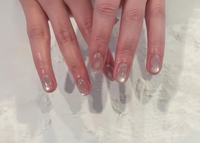 Close-up of hands with glittery nail polish on a textured white background