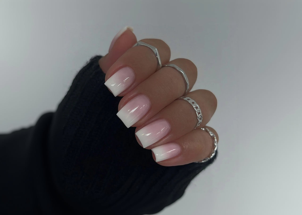 Close-up of a hand with pink and white nail polish and silver rings on a neutral background