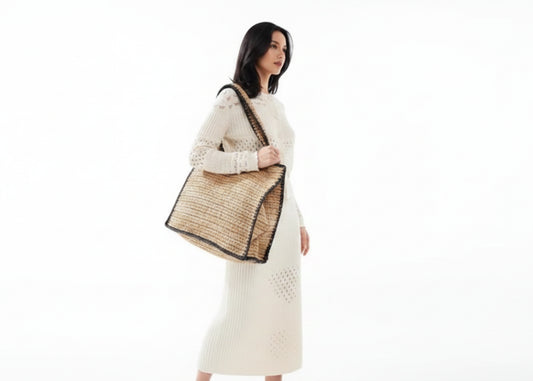 Beige woven bag with black trim on a white background, with a person holding it.