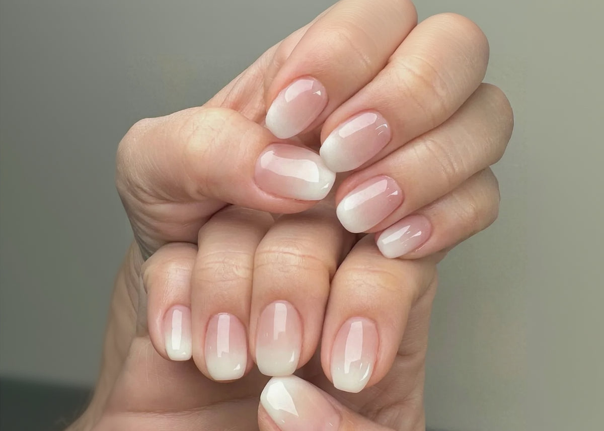Close-up of a hand with pink and white ombre nail polish on a neutral background