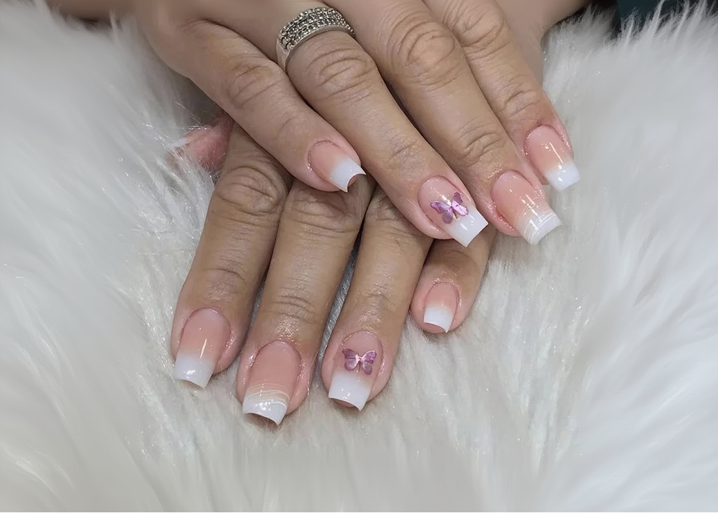 Close-up of hands with French manicure nails featuring butterfly designs on a textured surface.