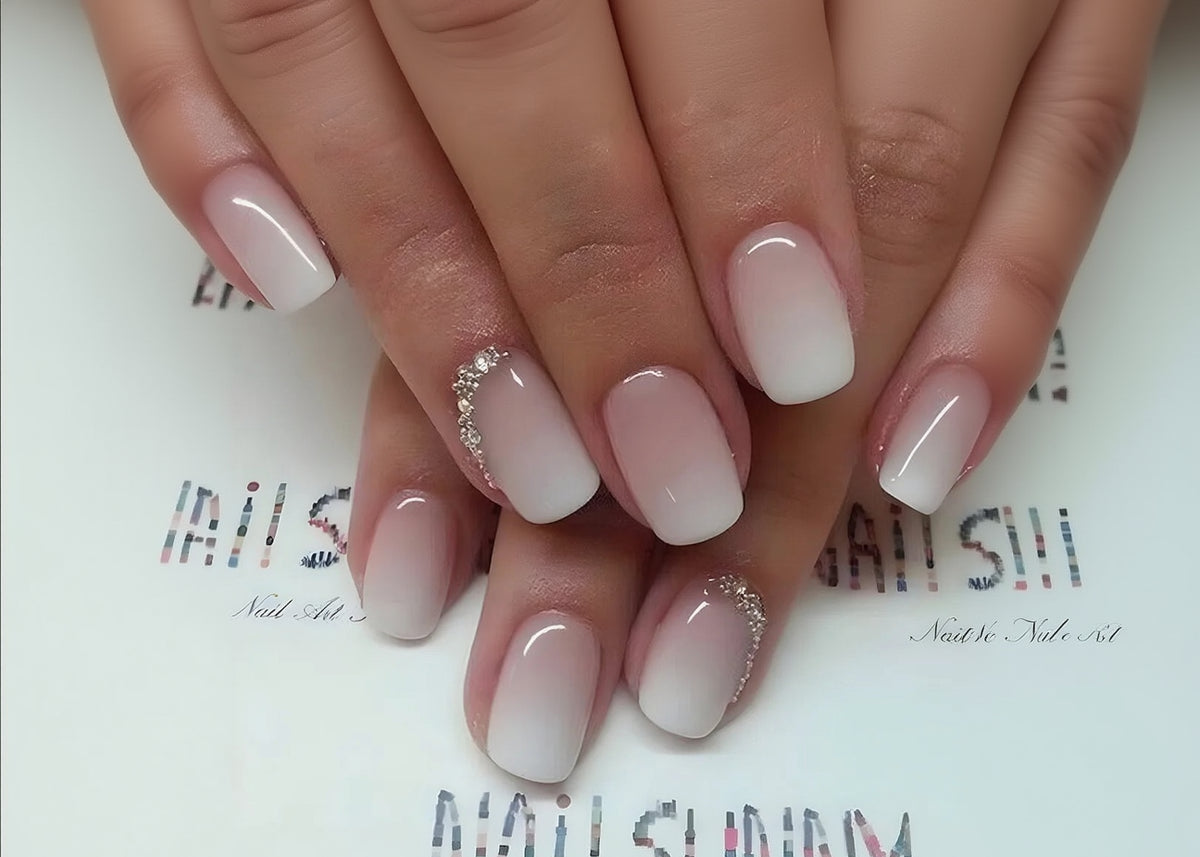Close-up of hands with white and pink gradient nail polish on a blurred background.