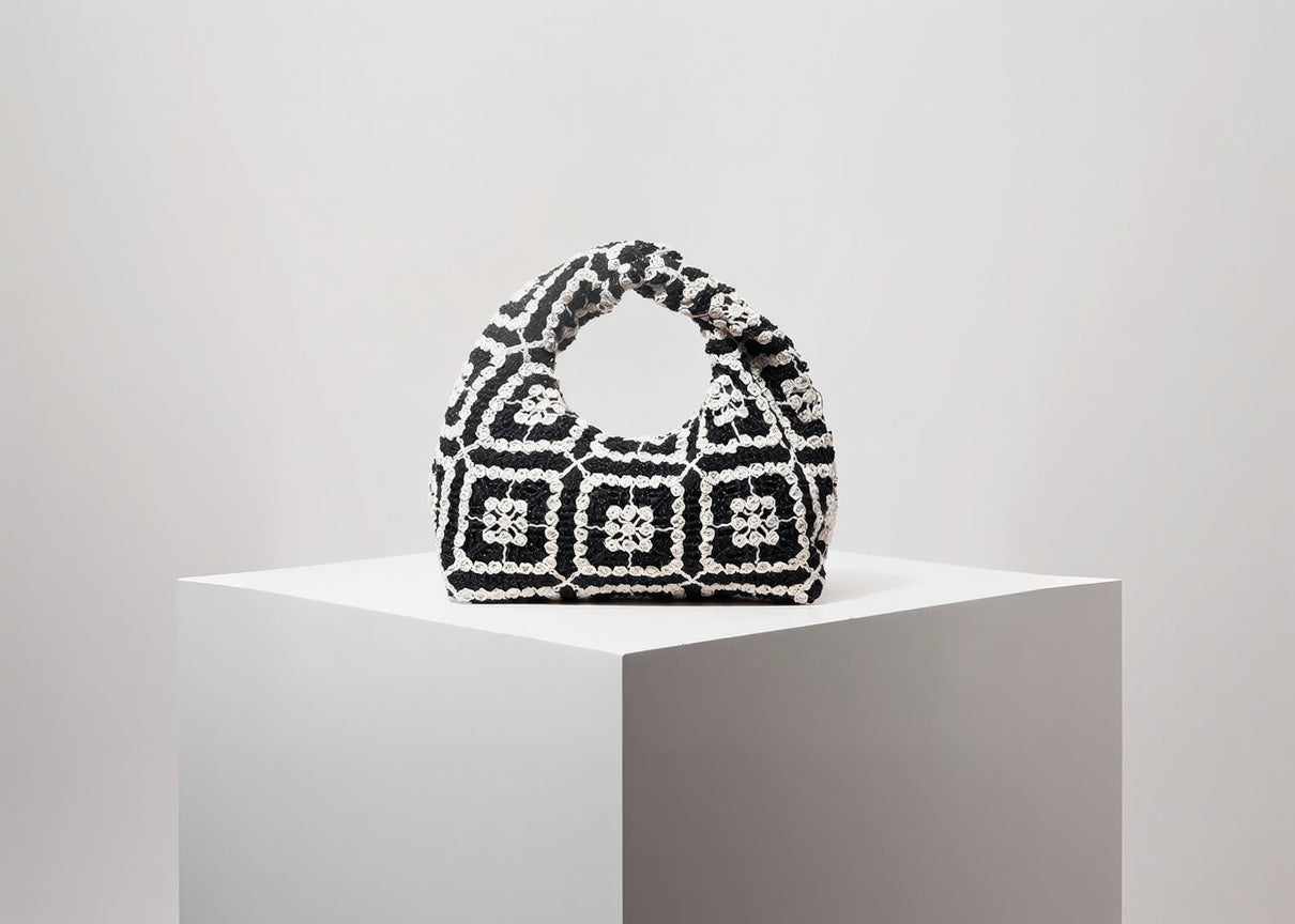 Black and white patterned handbag on a white pedestal with a light gray background