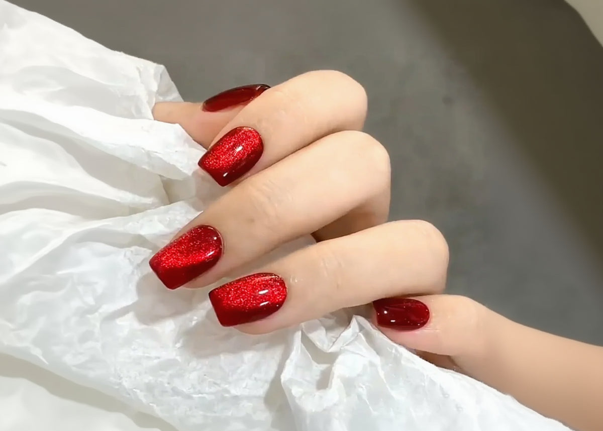 Hand with red glittery nail polish on a white fabric background