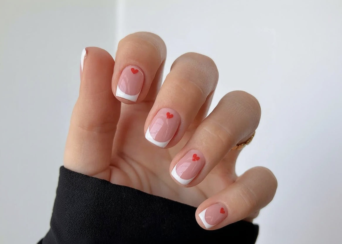 Close-up of a hand with pink nail polish and red heart designs on a white background