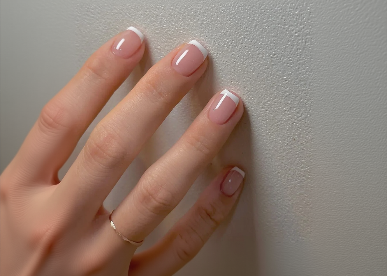Hand with pink nail polish on a plain background