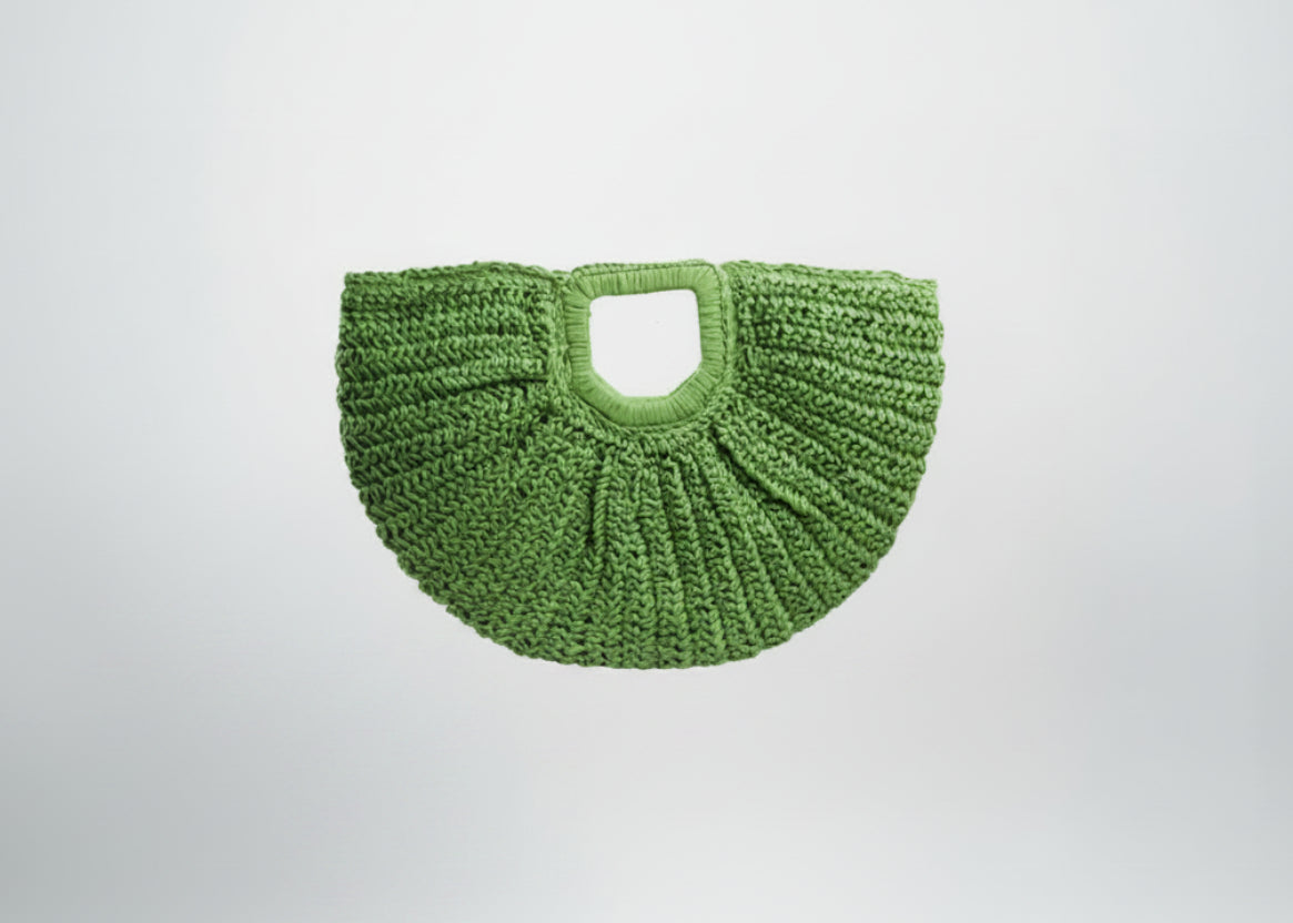 Green woven handbag held by a hand on a white background
