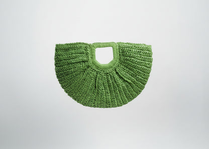 Green woven handbag held by a hand on a white background