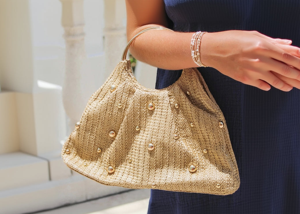 Beige woven handbag with pearl embellishments held by a person.
