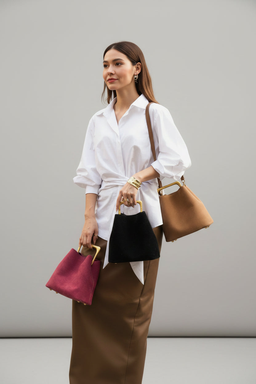 Person holding three handbags against a textured wall.