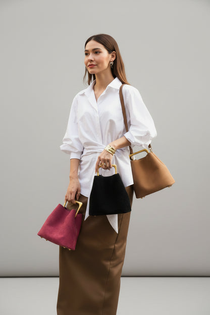 Person holding three handbags against a textured wall.