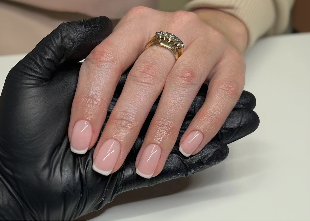 Hand with pink nail polish and a gold ring on a black surface