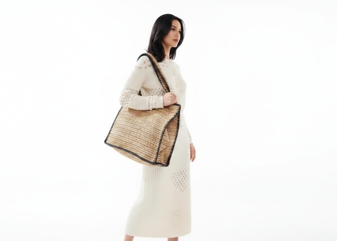 Beige woven bag with black trim on a white background, with a person holding it.