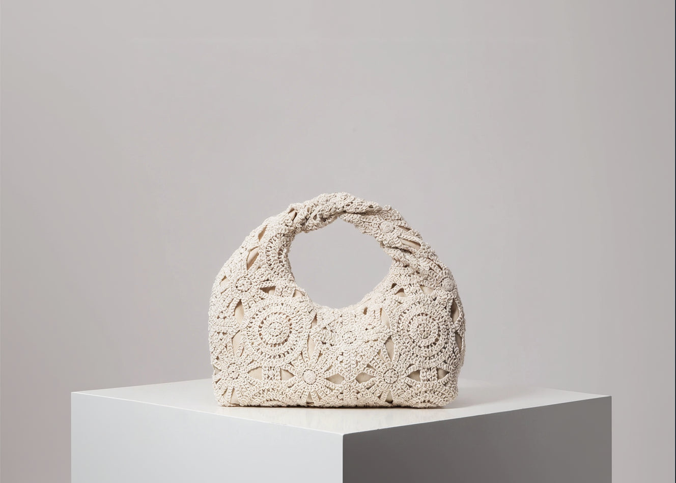 Beige crochet handbag on a white surface with a gray background