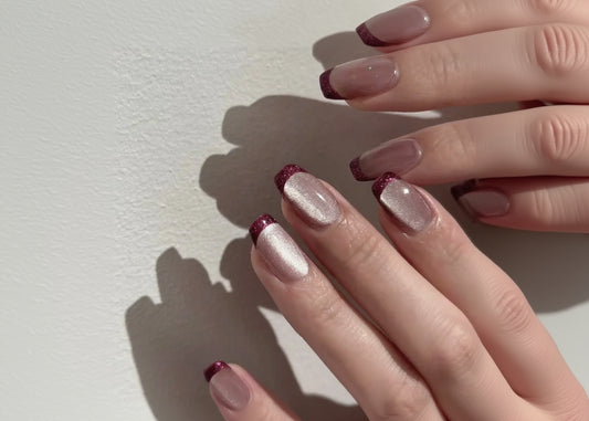Close-up of a hand with maroon and silver nail polish on a light background