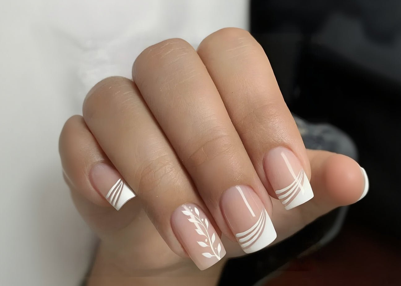 Close-up of a hand with pink nails featuring white decorative patterns.
