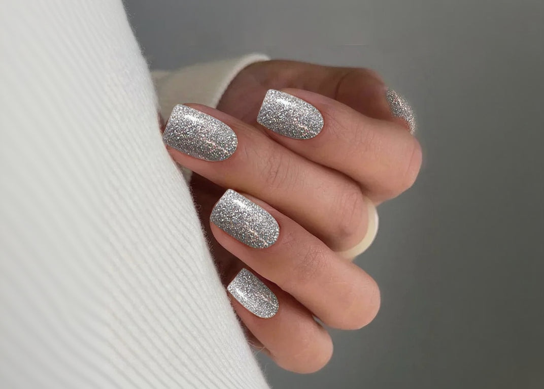 Close-up of a hand with silver glittery nail polish on a neutral background