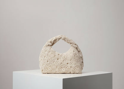 Beige crochet handbag on a white surface with a light gray background
