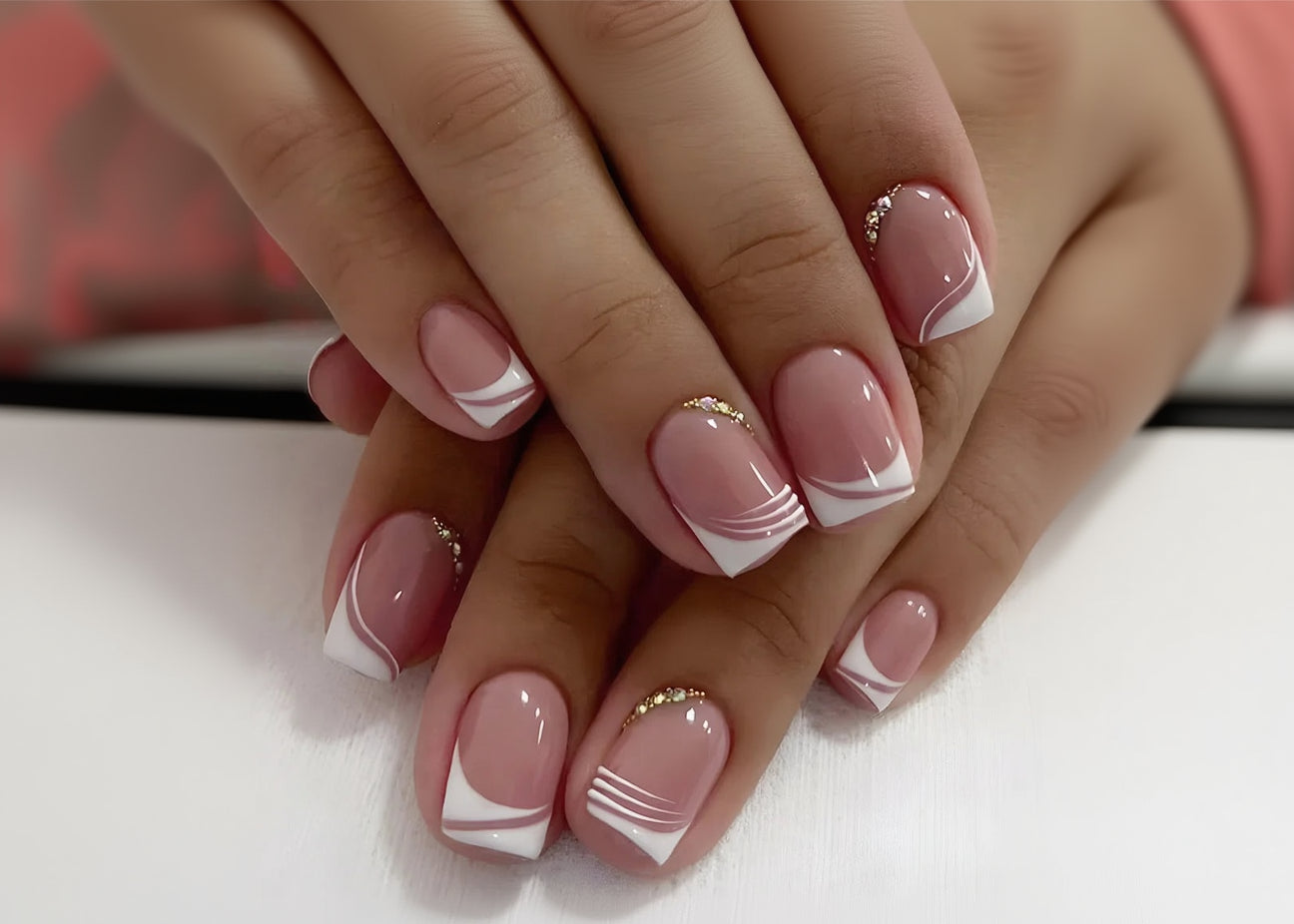 Close-up of hands with pink and white nail design on a light background