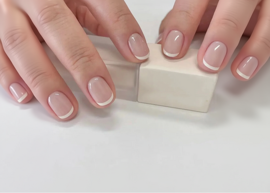 Close-up of hands with pink nail polish holding a small white cube.
