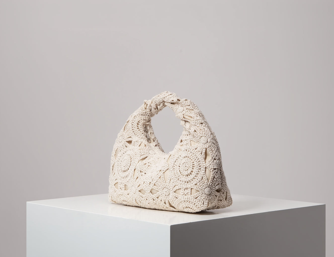 Crocheted handbag on a white pedestal against a gray background
