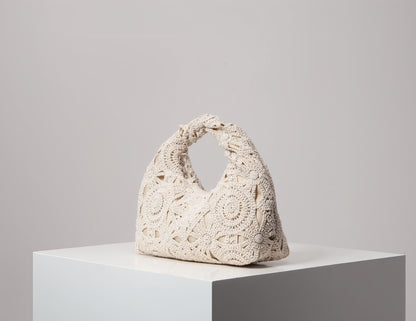 Crocheted handbag on a white pedestal against a gray background