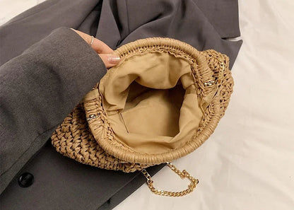 Woven handbag with gold chain held by a person wearing a gray coat on a light background