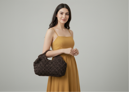 Person holding a brown woven handbag and a small bouquet of flowers indoors.
