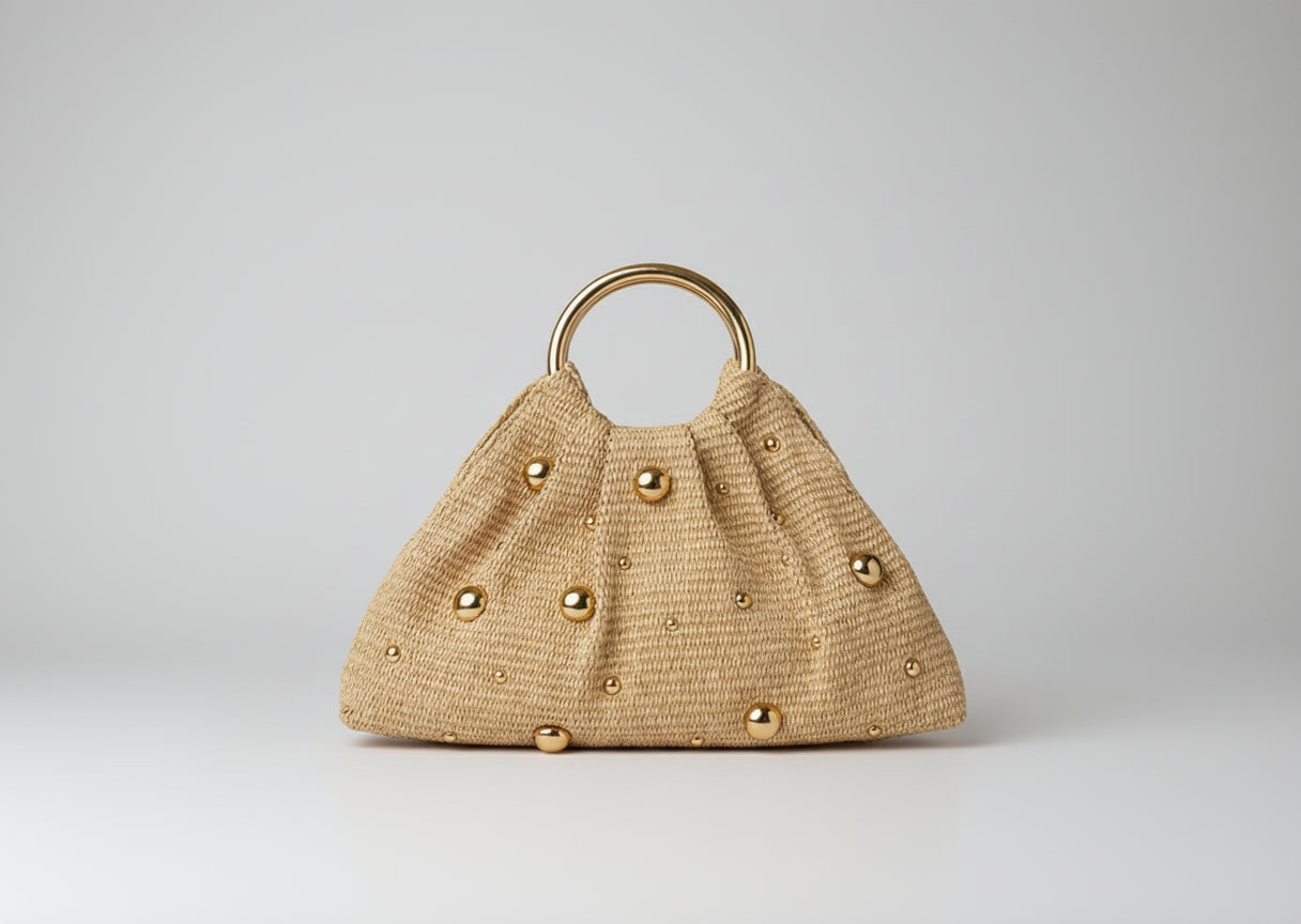 Beige handbag with gold buttons and handle on a beige couch