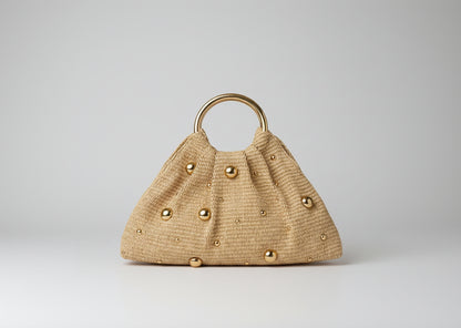 Beige handbag with gold buttons and handle on a beige couch