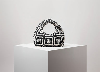 Black and white patterned handbag on a white pedestal with a light gray background