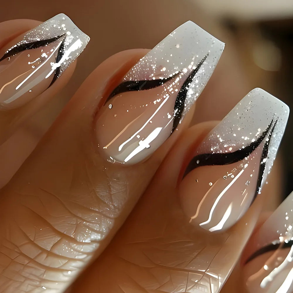 Close-up of a hand with long, white acrylic nails featuring black designs.