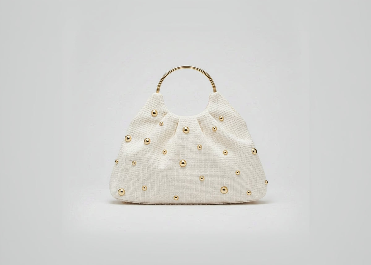 Beige handbag with gold studs on a white background