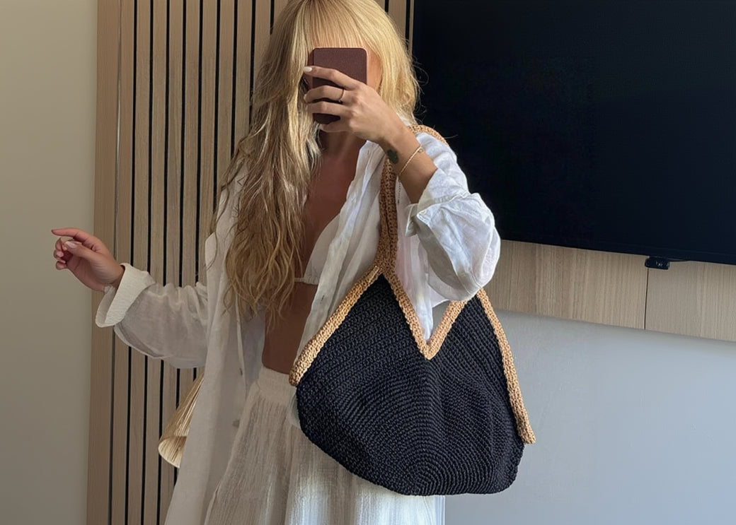 Person holding a black woven bag with beige trim