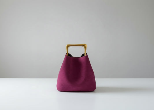Purple handbag with a gold handle on a wooden surface