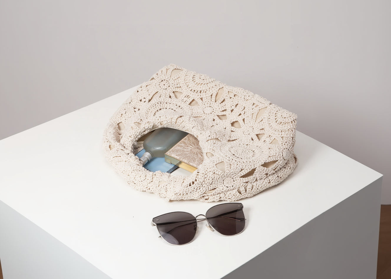 Crocheted bag with a sandal and sunglasses on a light surface