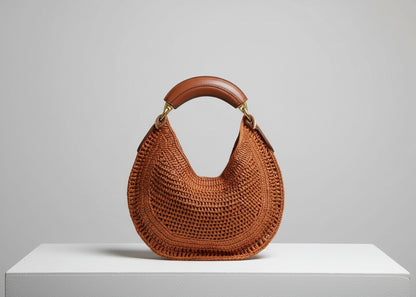 Brown woven handbag held by a person wearing a dark blue outfit.