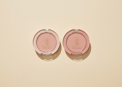 Four round Foremcos Forestyle makeup compacts in a row on a warm beige background, showing pressed powders in light pink, peach, coral, and deep berry tones.
